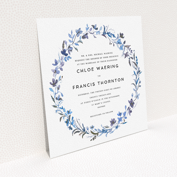 A personalised wedding invite design titled "Blue Floral Wreath". It is a square (148mm x 148mm) invite in a square orientation. "Blue Floral Wreath" is available as a flat invite, with tones of light blue, purple and grey.